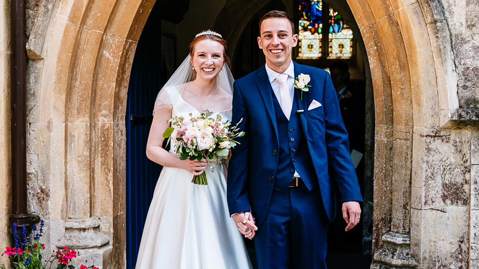Sarah and Daniel pictured in wedding attire stood in a doorway